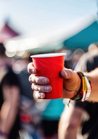 Man holding red papercup and wearing white empty paper wristband festival adult drink.
