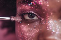 Super close up eye of black woman applying mascara on her lashes glitter cosmetics pink.