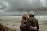 A photograph of an elderly couple standing on the beach sky photography shoreline.