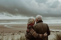 A photograph of an elderly couple standing on the beach cloud sky photography.