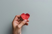 A heart shape paper cut model holding hand gray background.