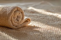 Calming and warm domestic scene with a focus on a neatly rolled-up light brown towel resting on a textured beige surface that appears to be a mat or tablecloth clothing knitwear blanket.