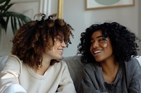 Two female friends sitting on a couch and talking accessories accessory laughing.