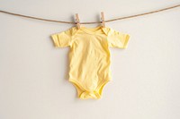 A pastel yellow newborn babysuit hang on rope with clothespin white background accessories coathanger.