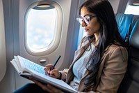 An Indian businesswoman sitting on an airplane seat and writing adult technology activity.