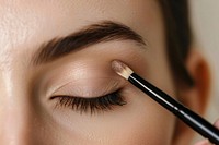 Woman applying biege eyeshadow brush cosmetics device.