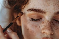 Woman applying biege eyeshadow brush cosmetics device.