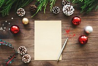 Festive Christmas scene with blank paper, surrounded by red and gold ornaments, pine cones, and green branches on a wooden table. Christmas decor and holiday decorations with copy space.