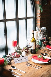 Festive table setting with wine, candles, and holiday decor. Reserved sign, wine glasses, and red accents create a cozy, festive atmosphere. Holiday decor and wine. Table reserved for Christmas dinner