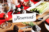 Festive table setting with a 'Reserved' sign. Holiday decor and pine cones on wooden table. Reserved sign on wooden table with Christmas decorations, foods and drinks. Reserved table on Christmas time.