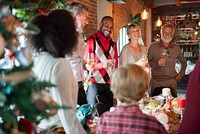 Group of diverse adults enjoying a festive gathering, holding drinks, smiling, and celebrating together in a warmly decorated room with holiday decor. Diverse family celebrating Christmas with dinner.