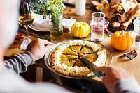 Pumpkin pie being sliced on a table with decorative pumpkins in Thanksgiving dinner. Warm autumn themed setting with people slicing pumpkin pie on wooden table. Thanksgiving pumpkin pie menu.