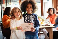 Diverse children smiling, holding a 'Happy Thanksgiving' card. Diverse kids, joyful moment, Thanksgiving celebration. Thanksgiving joy, diverse friendship. Diverse kids holding Thanksgiving card.