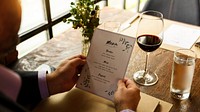 Man holding a menu at a restaurant table with a glass of red wine and water. Man reading menu with wine at the restaurant. Menu read by a man at restaurant's table with glass of wine and water.