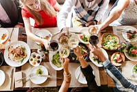 A group of people clinking glasses over a table filled with food. Celebratory atmosphere with diverse dishes and drinks. Friends enjoying a meal together. Clinking wine glasses, celebration toast.