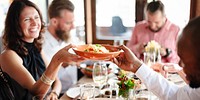 Group dining at a restaurant. Diverse people enjoying a meal of pasta. Smiling woman receiving a pasta dish. Social gathering with food, drinks, and conversation. Woman looking happy with the food.