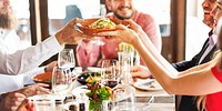 Group of diverse people enjoying a meal together at a restaurant. Smiling, sharing food, and socializing around a table with drinks and dishes. Diverse people socializing at sharing food at dinner.