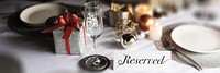 Elegant table setting with a reserved sign, featuring a gift box, glass, and festive decor. Perfect for a reserved, elegant, and festive occasion. Restaurant table reserved for holiday dinner.