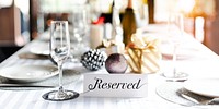 Elegant table setting with a 'Reserved' sign, wine glasses, and festive decor. The reserved table is ready for a special occasion with reserved seating. Table reserved for new years eve party.