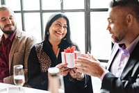 Group of people exchanging gifts at a celebration. Smiling woman receiving a present. Joyful atmosphere with friends sharing gifts and happiness. People exchanging holiday gifts.