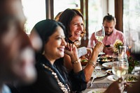 Friends enjoying a meal, diverse people smiling, holding wine glasses, sharing a joyful dining experience, cheerful atmosphere, enjoying together. Happy friends toasting and celebrating at restaurant.