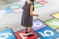 Child playing hopscotch on colorful numbered squares. Girl in dress, outdoor game, hopscotch fun. Bright numbers, playful activity, hopscotch joy. Child learning and playing.