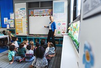 A teacher in a classroom with diverse children sitting on the floor. The teacher stands by a whiteboard, engaging students in a colorful, educational setting. Education and knowledge concept.