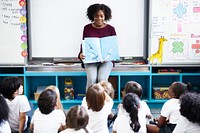 Teacher reading to diverse group of children. Classroom setting with teacher and students. Engaged children listening to teacher reading a book. Black teacher teaching nursery school class of children