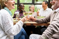 Group of diverse seniors enjoying a meal, laughing, and toasting with wine. Elderly friends, diverse gathering, joyful meal, and wine celebration. Seniors toasting with wine at luncheon.