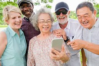 Group of diverse seniors enjoying time outdoors, looking at smartphone. Happy diverse elderly friends sharing joyful moment together at park. Diverse senior men and women look at phone happy in nature