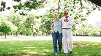 Elderly couple walking in a park, smiling and embracing. The elderly couple enjoys a sunny day, surrounded by trees, sharing a joyful moment outdoors. Happy elderly couple walking in the park.