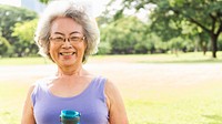 Senior woman outdoors, smiling in a park. She holds a water bottle, enjoying nature. Asian woman, gray hair, wearing glasses, embracing a healthy lifestyle. Senior Asian woman, wellness in park.