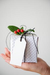 Hand holding a small, wrapped gift with a blank tag. Perfect for holiday gift ideas and gift-giving inspiration. Christmas gift on white background with a blank tag copy space. 