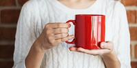 Person holding a large red mug, wearing a white sweater. Close-up of hands with a red mug. Red mug and sweater create a cozy, warm vibe. Woman holding a warm drink in winter.