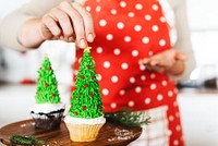 Festive cupcakes decorated as Christmas trees. A person in a red polka dot apron adds final touches. Holiday cupcakes, Christmas trees, festive baking. Festive Christmas tree cupcakes.