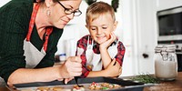 A woman and child bake cookies together. The woman decorates cookies, while the child watches. Baking cookies is a fun activity for them both. Mother and son baking for Christmas.