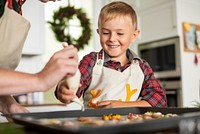 A cheerful young Caucasian boy in a plaid shirt enjoys baking cookies with a caregiver. The boy smiles as they decorate cookies together, creating festive treats in a cozy kitchen.