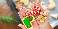 Hands holding festive cookies: a candy cane, a gingerbread man, and a stocking. Colorful holiday cookies, perfect for Christmas celebrations and festive treats. Christmas baking activity for kids.