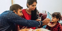 Indian family dining together, parents feeding child. Indian family enjoying meal, sharing food. Parents and child at table, bonding over dinner. Family time, sharing moments. happy Indian family.