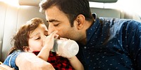 Father and child in a car. South Father kisses child. Child drinks from a bottle. Loving father, caring father, affectionate father. Family moment. Father and kid along the family trip in car.