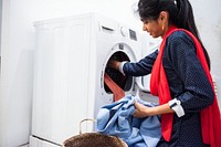 Indian woman doing laundry, placing clothes in a washing machine. Laundry, washing clothes, using washing machine. Household chores, Indian woman doing laundry at home. Woman doing household chores.