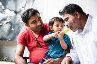 A Indian child feeds a man a slice of fruit while another Indian man watches. The scene captures a moment of care and connection between the three individuals. Indian family with child and dad.