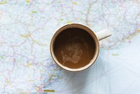 A coffee cup on a map, showing a journey. The coffee cup is centered, highlighting travel, exploration, and adventure. Perfect for travel enthusiasts. Coffee cup on map background. Travel background.