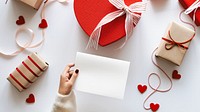 Gift boxes and a heart-shaped box with ribbons. A hand holds a blank card for Valentines or romantic occasions. Brown and red Valentines gift boxes and hand holding card. Valentines paper gift boxes.