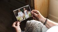 Senior hands holding a photo of a couple in a field. The couple is dressed in wedding attire. The photo evokes nostalgia and memories of a special day. Senior woman remembering husband in photo.