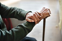 Close-up of elderly hands resting on a cane, symbolizing aging and support. The hands show wrinkles and veins, emphasizing age and experience. Elderly man with cane. Healthcare and wellness concept.