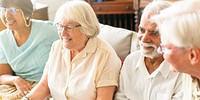 Group of diverse senior friends sitting on a couch, smiling and watching TV together. Diverse senior group enjoying time and companionship together. Senior friendship and retirement life. 