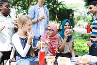 Group of diverse friends enjoying a picnic outdoors, eating sandwiches and drinking soda. Multicultural gathering with food, laughter, and nature. Diverse friends having picnic in park.