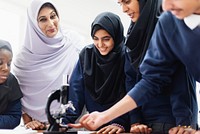 Group of students and a teacher in hijabs and uniforms, gathered around a microscope, engaged in a science lesson, collaborative learning environment. Young Muslim girl wearing hijab in school.