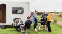 Diverse group of senior friends enjoying barbecue by a caravan. Outdoor gathering with friends. Relaxing near a caravan, cooking and chatting. Casual outdoor senior friends barbecue scene.